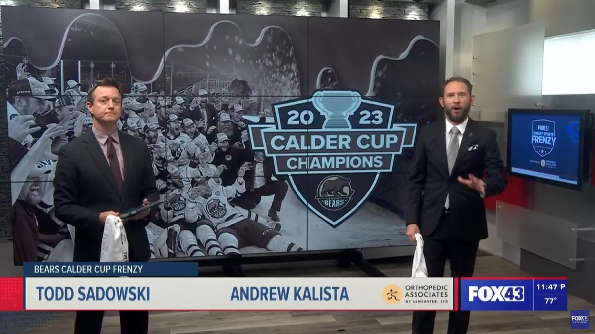 Todd Sadowski and Andrew Kalista from FOX43 stand in front of an image of the Hershey Bears celebrating their 2023 Calder Cup championship win. There is a 2023 Calder Cup Champions and Hershey Bears logo over the image of the team.
